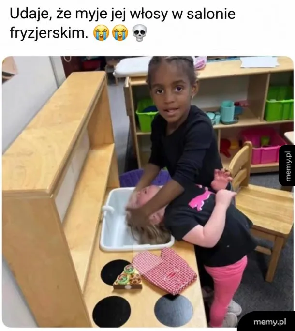 Dziewczynka udaje, że myje włosy drugiej koleżance w zabawkowym zlewie.
