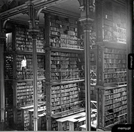Czarno-białe zdjęcie ogromnej, wielopoziomowej biblioteki z wysokimi regałami pełnymi książek.