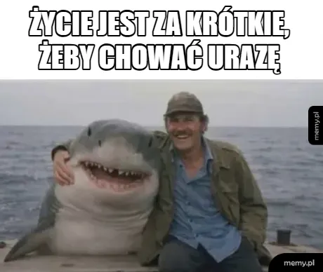 Mężczyzna obejmuje ramieniem uśmiechniętego rekina siedzącego na pomoście.